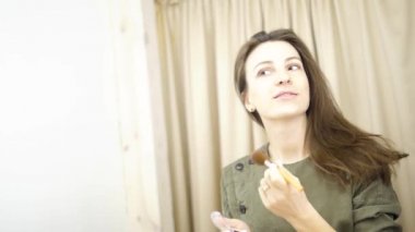 Makyaj yapan bir kadın. Güzel kız aynaya bakıyor ve büyük bir fırçayla kozmetik uyguluyor. Kızın elmacık kemikleri kızarıyor. Pudra, allık.