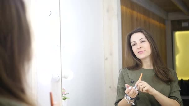 Mujer de belleza aplicando maquillaje. Hermosa chica mirándose en el espejo y aplicando cosméticos con un cepillo grande. La chica se sonroja en los pómulos. Polvo, colorete — Vídeo de stock