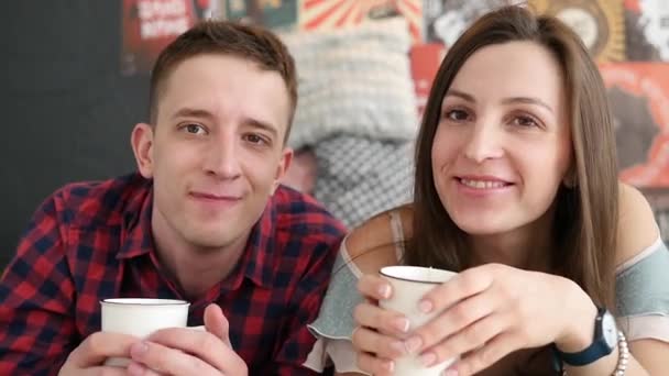 若いカップルがベッド、幸せな笑顔の女性男性恋人愛ロマンチックな朝スローモーションでコーヒーを飲む — ストック動画