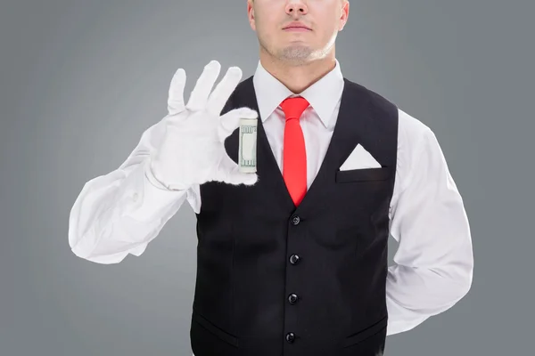Handsome young waiter in gloves and red cravat holding money — Stock fotografie