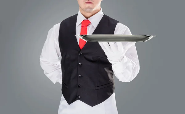 Guapo joven camarero en guantes y cravat rojo sosteniendo bandeja vacía —  Fotos de Stock