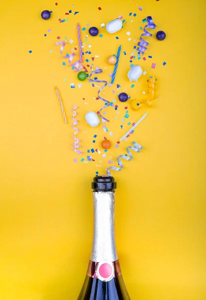 Kleurrijke partij kenmerken vliegen uit van botle van champagne wijn. op een gele achtergrond. Plat liggen. Vieren concept. Hoge resolutie foto. — Stockfoto