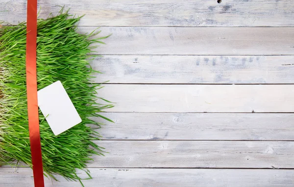 Rote Dekorationslinie mit Schleife auf einem Gras auf einer gebürsteten weißen Holzplatte. Geschenke oder Feierkokett. flache Lage. — Stockfoto