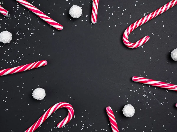 Καραμέλες σε σχήμα κύκλου σε μαύρο φόντο με άσπρες μπάλες καρύδας και κλαδιά ελάτης. Χριστουγεννιάτικη κάρτα. Καλή Χρονιά. — Φωτογραφία Αρχείου