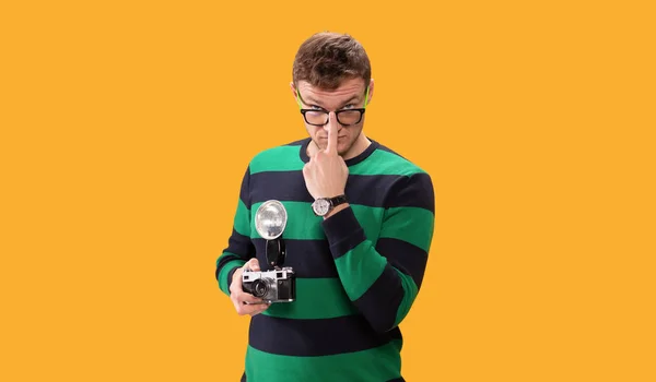 Студийный портрет красивого молодого человека держит фотокамеру, фотографирующую. Брюнетка регулирует очки на носу. Желтый покров . — стоковое фото