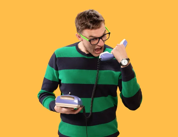 Angry young man talking on the phone. Man holds purple phone in his hands and calling on a yellow background. Studio photo. — 스톡 사진