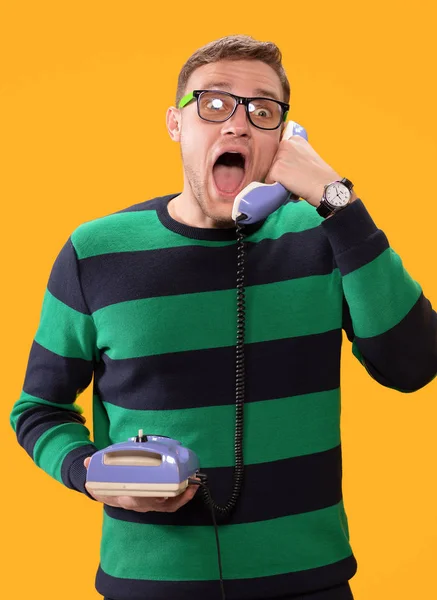 Arg ung man pratar i telefon. Mannen håller lila telefon i sina händer och kallar på en gul bakgrund. Mannen med öppen mun skriker i telefonen. Studiofoto. — Stockfoto