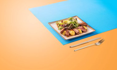 Soslu biftek, patates ve yeşil salata. Renkli, güneşli bir arka plan. Avrupa yemekleri için lezzetli menü.