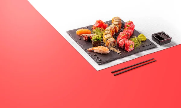 Different types of sushi are served on a black plate. Colorful sunny background. Sushi menu for japanese food. Japanese sushi set. — Stock Photo, Image