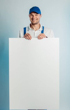 Elinde boş beyaz pankart tutan genç bir gülen işçi resmi. Beyaz ya da mavi arka plan. İş konsepti.