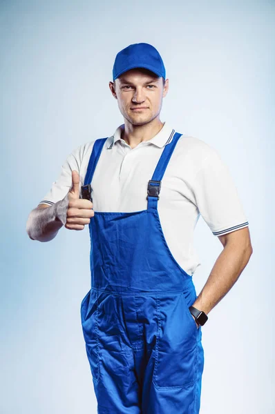 Portrait of young worker man wearing blue uniform. Showing thumb up. Movement cool. Isolated on grey background with copy space. Human face expression, emotion. Business concept. — 스톡 사진