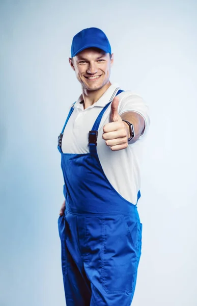 Retrato de jovem trabalhador usando uniforme azul. A mostrar o polegar. Movimento fixe. Isolado em fundo cinza com espaço de cópia. Expressão facial humana, emoção. Conceito de negócio . — Fotografia de Stock