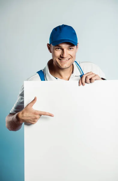 Mockup image of a young smiling worker holding empty white banner and points to it. — Stock Photo, Image