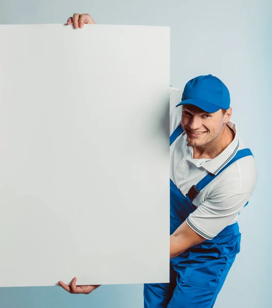Imagem falsa de um jovem trabalhador sorrindo segurando uma bandeira branca vazia. Fundo branco ou azul. Conceito de negócio . — Fotografia de Stock