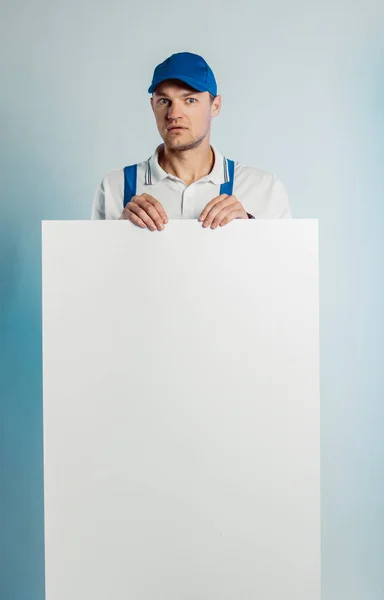 Imagem falsa de um jovem trabalhador surpreso segurando uma bandeira branca vazia. Fundo branco ou azul. Conceito de negócio . — Fotografia de Stock