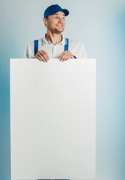 Imagem falsa de um jovem trabalhador a segurar uma bandeira branca vazia. Fundo branco ou azul. Conceito de negócio . — Fotografia de Stock