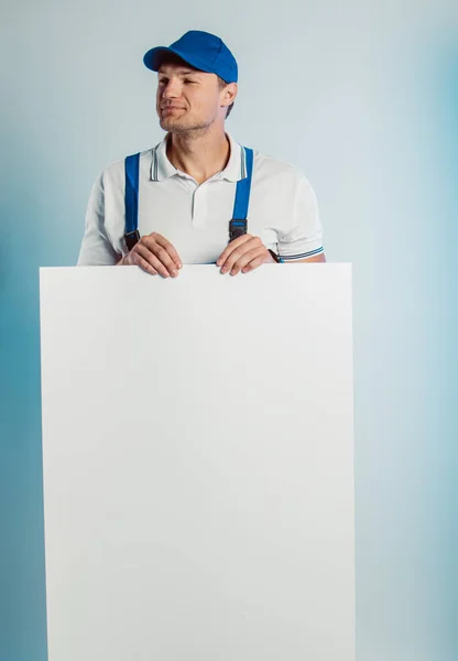 Imagen burlona de un joven trabajador pensativo sosteniendo una pancarta blanca vacía. Fondo blanco o azul. Concepto empresarial . — Foto de Stock