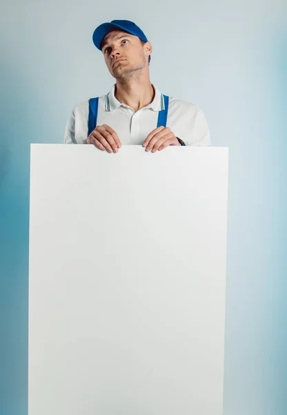 Imagem falsa de um jovem trabalhador pensativo segurando uma bandeira branca vazia. Fundo branco ou azul. Conceito de negócio . — Fotografia de Stock