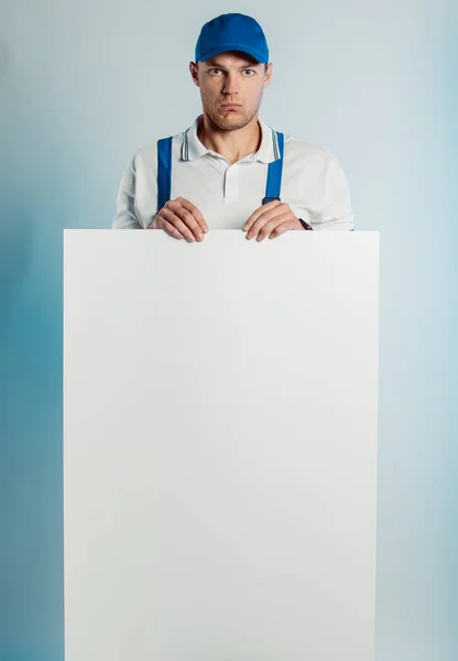 Imagem falsa de um jovem trabalhador discursado segurando uma bandeira branca vazia. Fundo branco ou azul. Conceito de negócios . — Fotografia de Stock