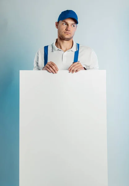 Imagem falsa de um jovem trabalhador pensativo segurando uma bandeira branca vazia. Fundo branco ou azul. Conceito de negócio . — Fotografia de Stock