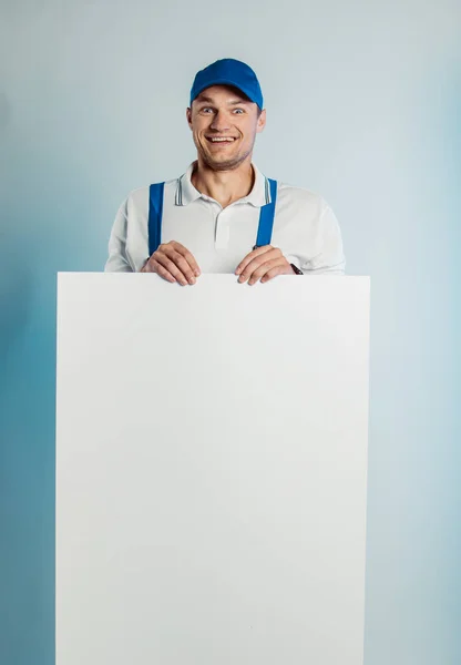 Imagen burlona de un joven trabajador sonriente con una pancarta blanca vacía. Fondo blanco o azul. Concepto de empresas . — Foto de Stock