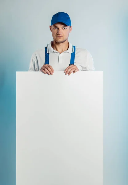 Imagen burlona de un joven trabajador pensativo sosteniendo una pancarta blanca vacía. Fondo blanco o azul. Concepto de empresas . — Foto de Stock