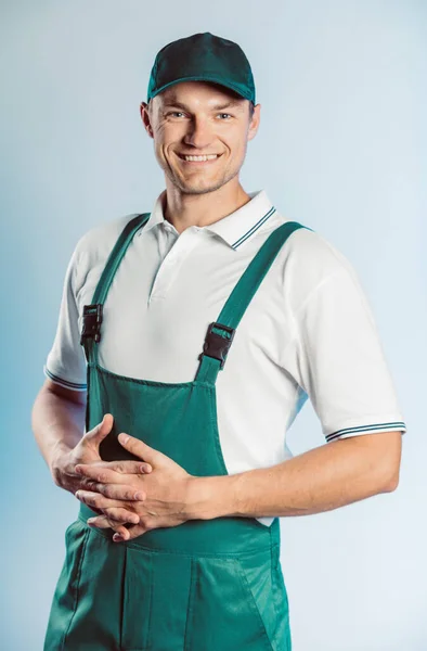 Retrato de un joven trabajador vestido de uniforme verde con las manos cruzadas. Aislado sobre fondo gris con espacio de copia. Expresión de rostro humano, emoción. Concepto empresarial . — Foto de Stock