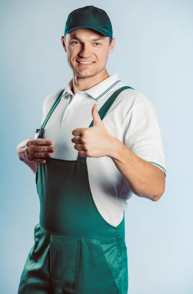 Portrait of young worker man wearing green uniform. Showing thumb up. Movement cool. Isolated on grey background with copy space. Human face expression, emotion. Business concept. — Stock Photo, Image