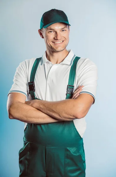 Retrato de un joven trabajador vestido de uniforme verde con las manos cruzadas. Aislado sobre fondo gris con espacio de copia. Expresión de rostro humano, emoción. Concepto empresarial . — Foto de Stock