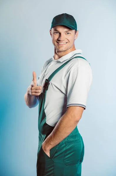 Retrato de un joven trabajador con uniforme verde. Apuntando con el dedo hacia ti mirando la cámara. Aislado sobre fondo gris con espacio de copia. Expresión de rostro humano, emoción. Concepto empresarial . — Foto de Stock