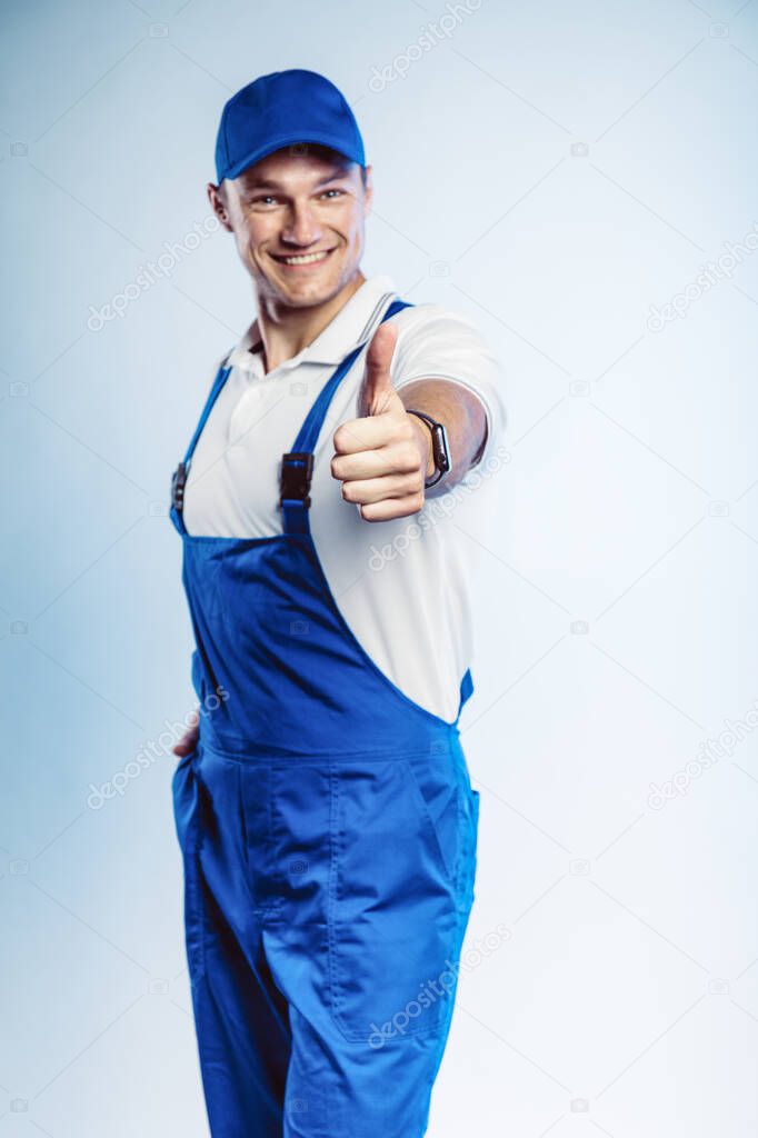 Portrait of young worker man wearing blue uniform. Showing thumb up. Movement cool. Isolated on grey background with copy space. Human face expression, emotion. Business concept.