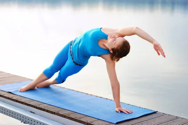 Yoga girl practicing side plank positing at the river bank in th