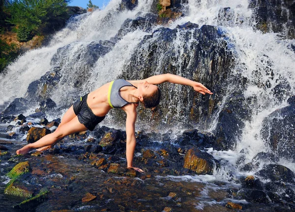 Yoga girl practicing side plank position under the waterfall hor