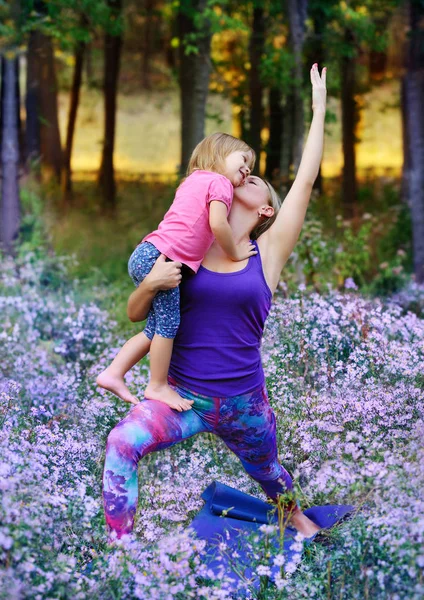Mother kissing her daughter practicing warrior yoga pose in the