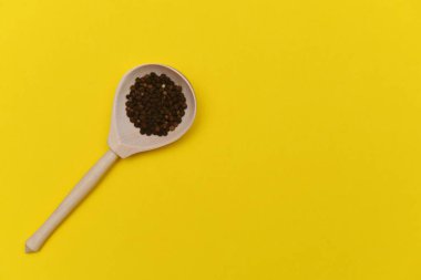 Sarı arka planda tahta kaşıkta biber.