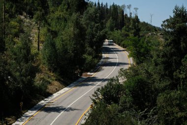 Araba, dağlık bir bölgede dolambaçlı bir yol boyunca gidiyor.