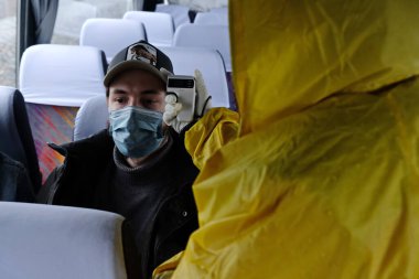 Almaty / Kazakistan - 04.09.2020: Bir sağlık görevlisi otobüs yolcularının sıcaklığını kontrol ediyor