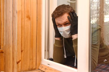 Koruyucu maskeli ve eldivenli bir adam ellerini başının yanında tutuyor.