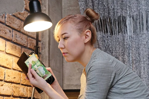 The girl holds in her hands and looks at the banknote with the face value of 2000 tenge