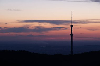 Kok Tobe TV kulesi, yüksek bir tepede, Kazakistan 'ın Almatı şehrinin üzerindeki ağaçlarla birlikte. Gün batımından sonra.