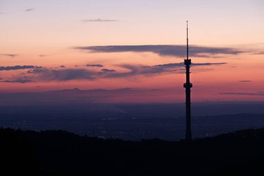 Kok Tobe TV kulesi, yüksek bir tepede, Kazakistan 'ın Almatı şehrinin üzerindeki ağaçlarla birlikte. Gün batımından sonra.