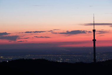 Kok Tobe TV kulesi, yüksek bir tepede, Kazakistan 'ın Almatı şehrinin üzerindeki ağaçlarla birlikte. Gün batımından sonra.