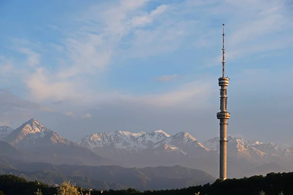 Kok Tobe TV kulesi, yüksek bir tepede, Kazakistan 'ın Almatı şehrinin üzerindeki ağaçlarla birlikte. Akşam vakti, gün batımından önce