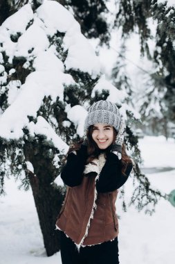 Genç bir kadın kışın karlı bir parkta yürümekten zevk alıyor.
