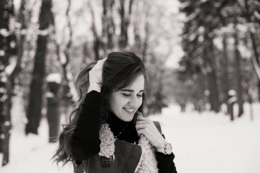 Genç bir kadın kışın karlı bir parkta yürümekten zevk alıyor.