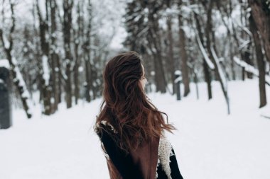 Genç bir kadın kışın karlı bir parkta yürümekten zevk alıyor.