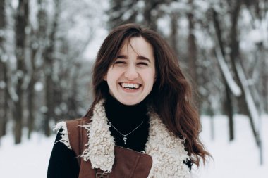 Genç bir kadın kışın karlı bir parkta yürümekten zevk alıyor.