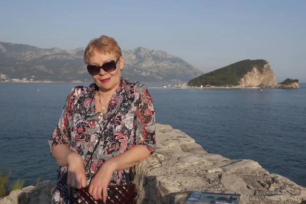 Olgun bir kadın arka planda Sveti Stefan Adası
