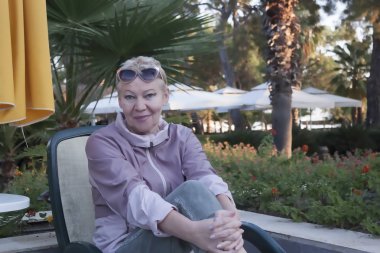 Alnında güneş gözlüğü olan olgun bir kadın gülümsüyor.