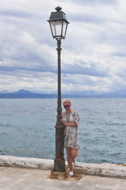 Olgun bir kadın fenerin yanındaki güvertede duruyor. Yaz bulutlu günü
